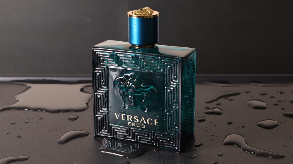 Une bouteille bleue de parfum Versace posée sur une surface noire.
