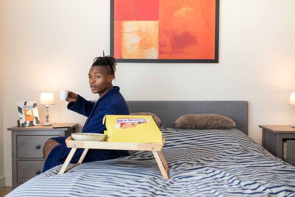 Un homme assis sur un plateau devant un lit.