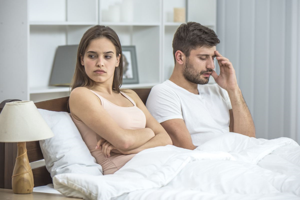 Un homme et une femme assis au lit et parlant au téléphone.