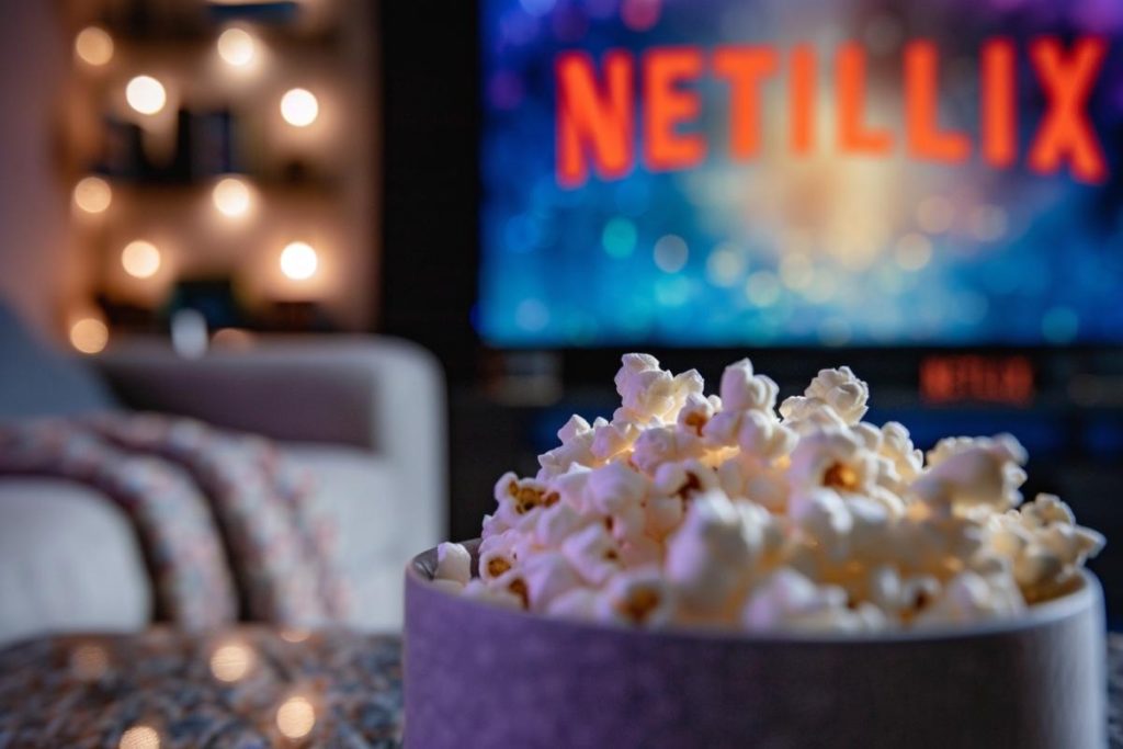 Un bol de pop-corn au premier plan avec un écran de télévision flou affichant « NETILLIX » en arrière-plan.