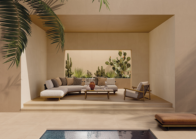 Patio extérieur moderne avec des murs beiges, un canapé sectionnel, un fauteuil, une table basse et des cactus en arrière-plan, au bord d'une piscine.