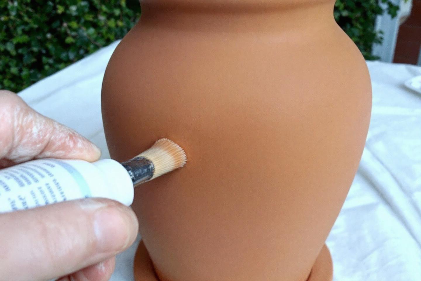 Main tenant un pinceau contre un vase en terre cuite