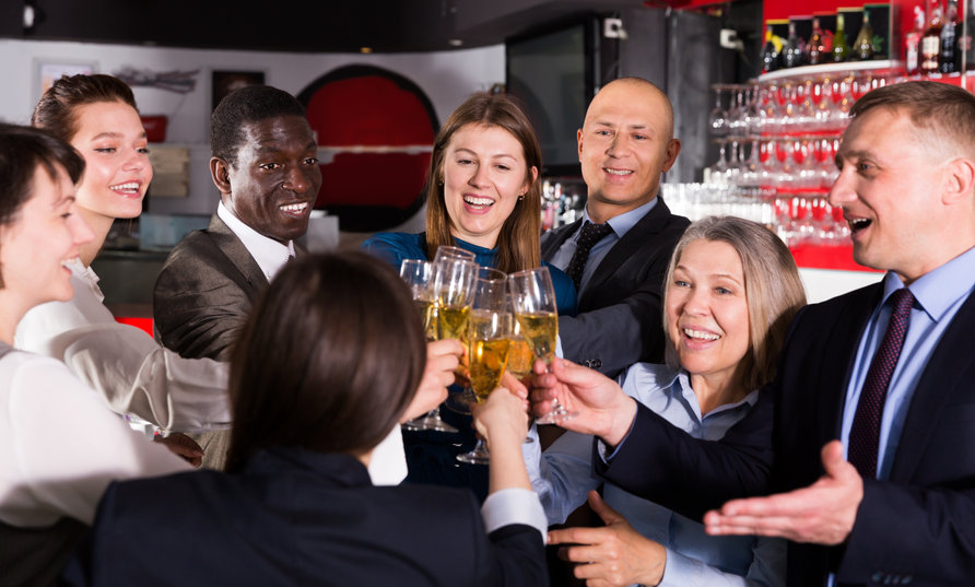 Groupe de personnes habillées professionnellement qui lèvent leur verre pour porter un toast et sourient dans un bar ou un restaurant.
