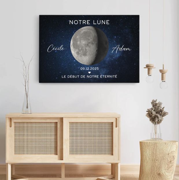 Une estampe encadrée représentant une demi-lune dans un ciel étoilé, avec les noms Cécile et Adam, une date et un texte en français, suspendue au-dessus d'un meuble en bois clair dans une pièce moderne.
