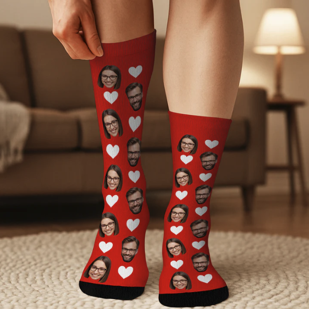 Personne portant des chaussettes rouges avec des cœurs blancs et des visages imprimés d'un homme et d'une femme, debout sur le sol moquetté d'un salon.