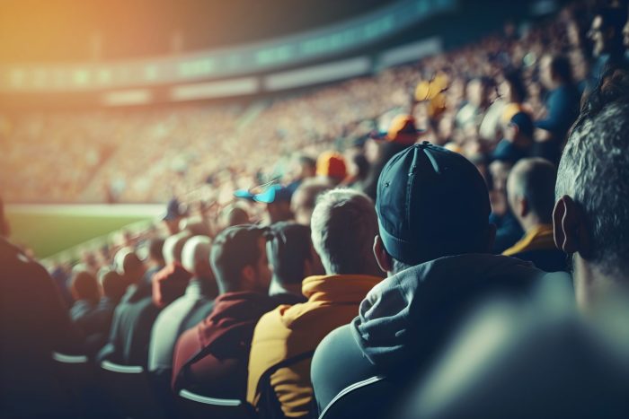 Une foule de spectateurs est assise dans un stade, regardant un événement sur le terrain sous des lumières vives avec des sièges flous en arrière-plan.