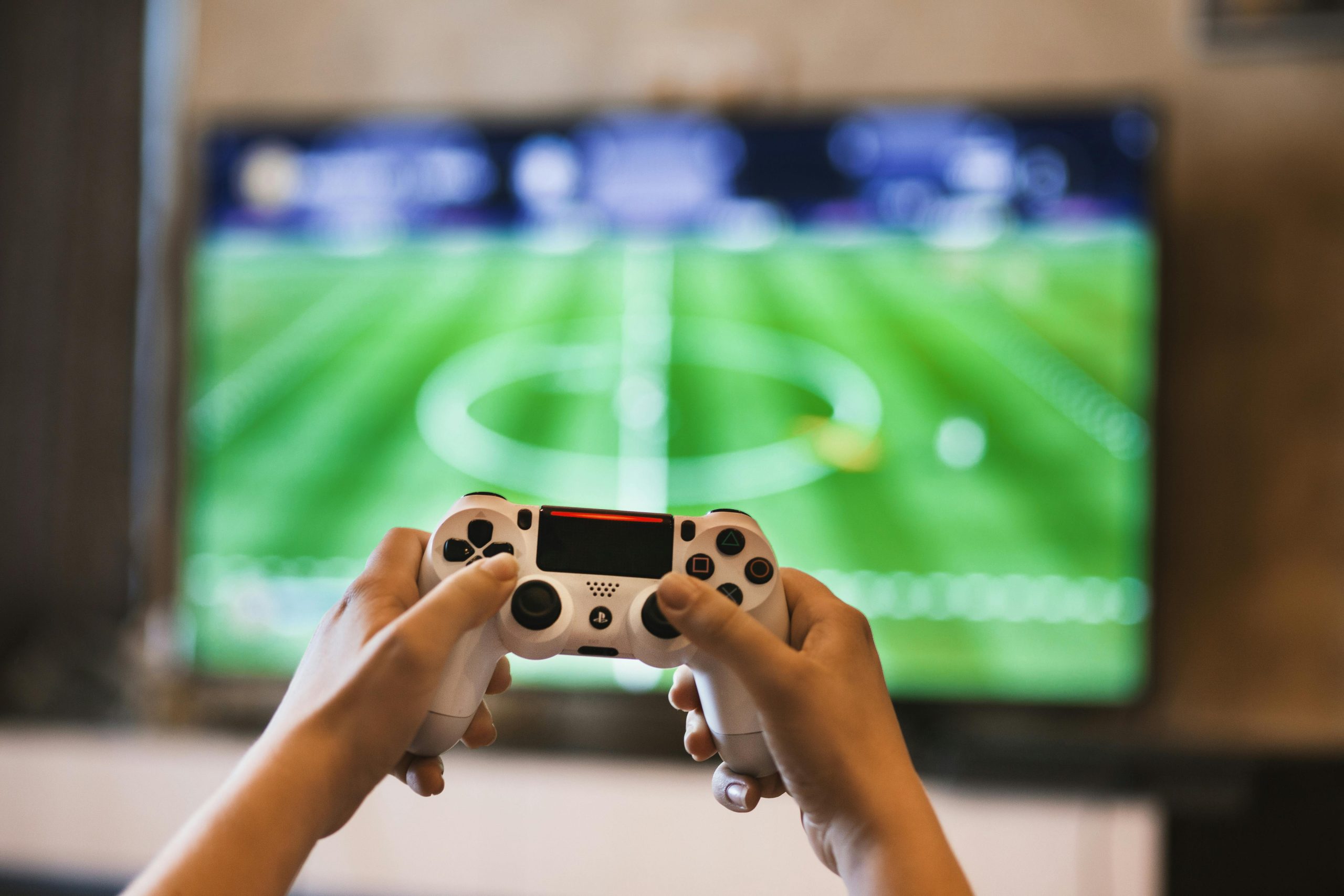 Personne tenant une manette de jeu vidéo tout en jouant à un jeu vidéo de football sur un grand écran de télévision.