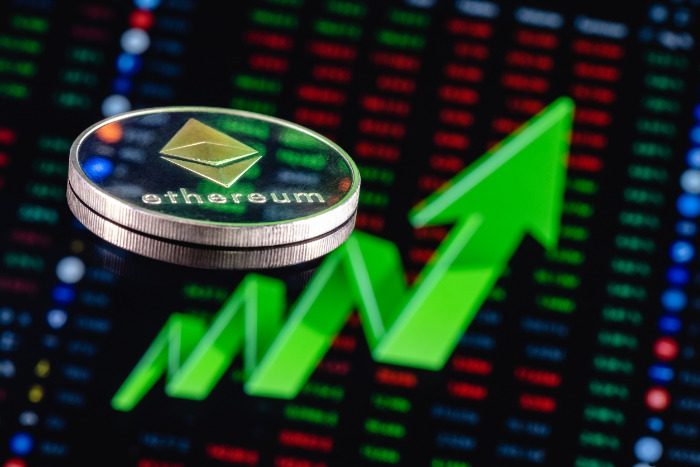 Pièce d'Ethereum devant un tableau boursier numérique avec une grande flèche verte vers le haut, indiquant une valeur en hausse ou une croissance positive.