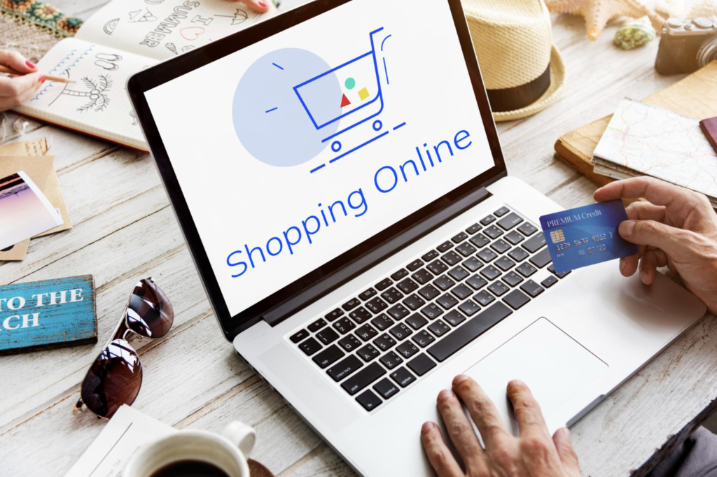 Une personne utilise un ordinateur portable affichant un écran "Shopping en ligne" et tient une carte de crédit, avec divers articles sur une table en bois.