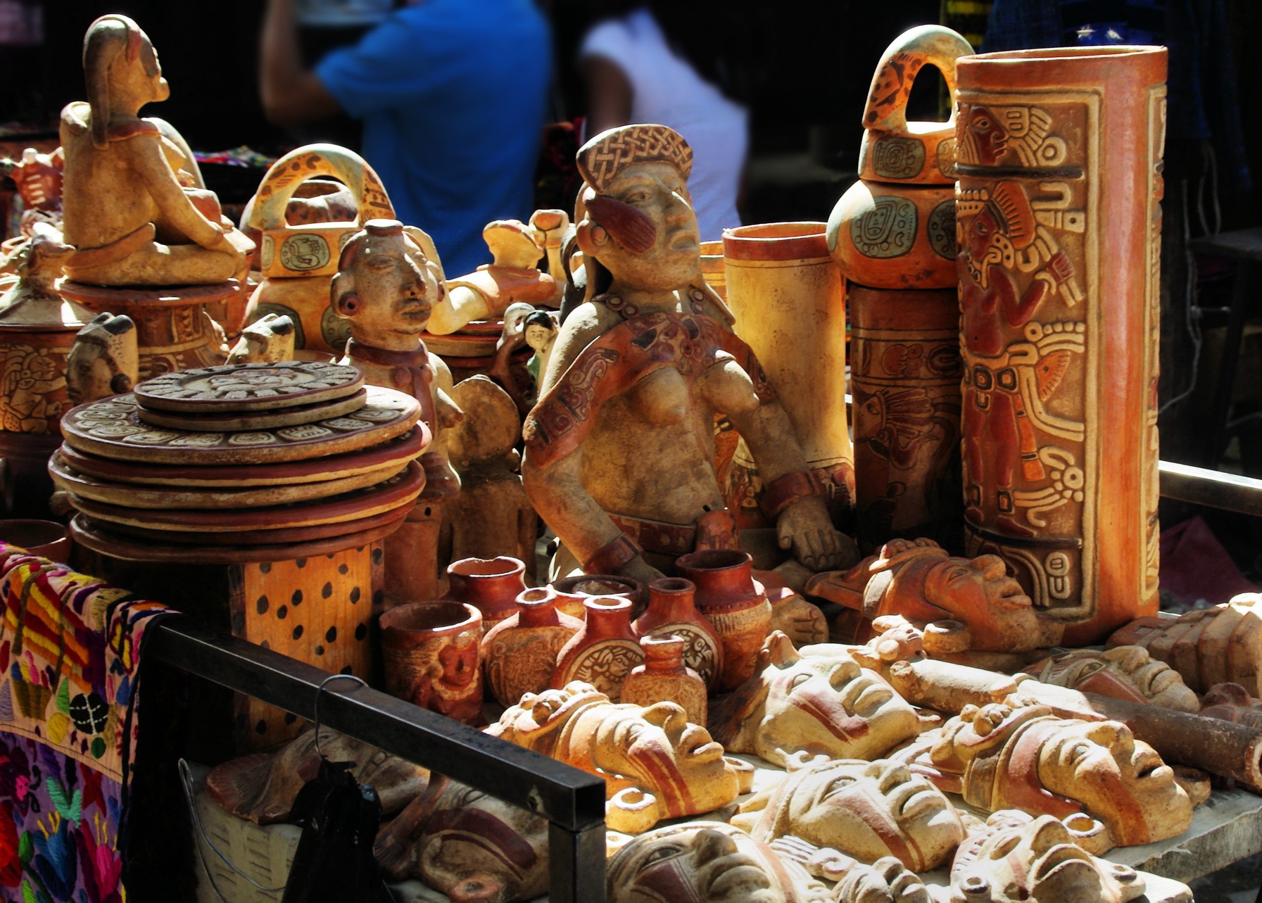 Présentation sur une table de diverses figurines en argile sculptées et peintes, d’assiettes et d’objets décoratifs, probablement sur un étal de marché.