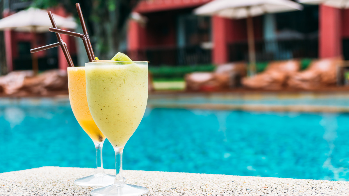 Deux cocktails posés au bord d'une piscine avec des transats en arriere plan.
