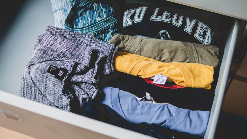 Un tiroir rempli de t-shirts pliés, dont un t-shirt bleu marine sur lequel est imprimé « KU LEUVEN ».