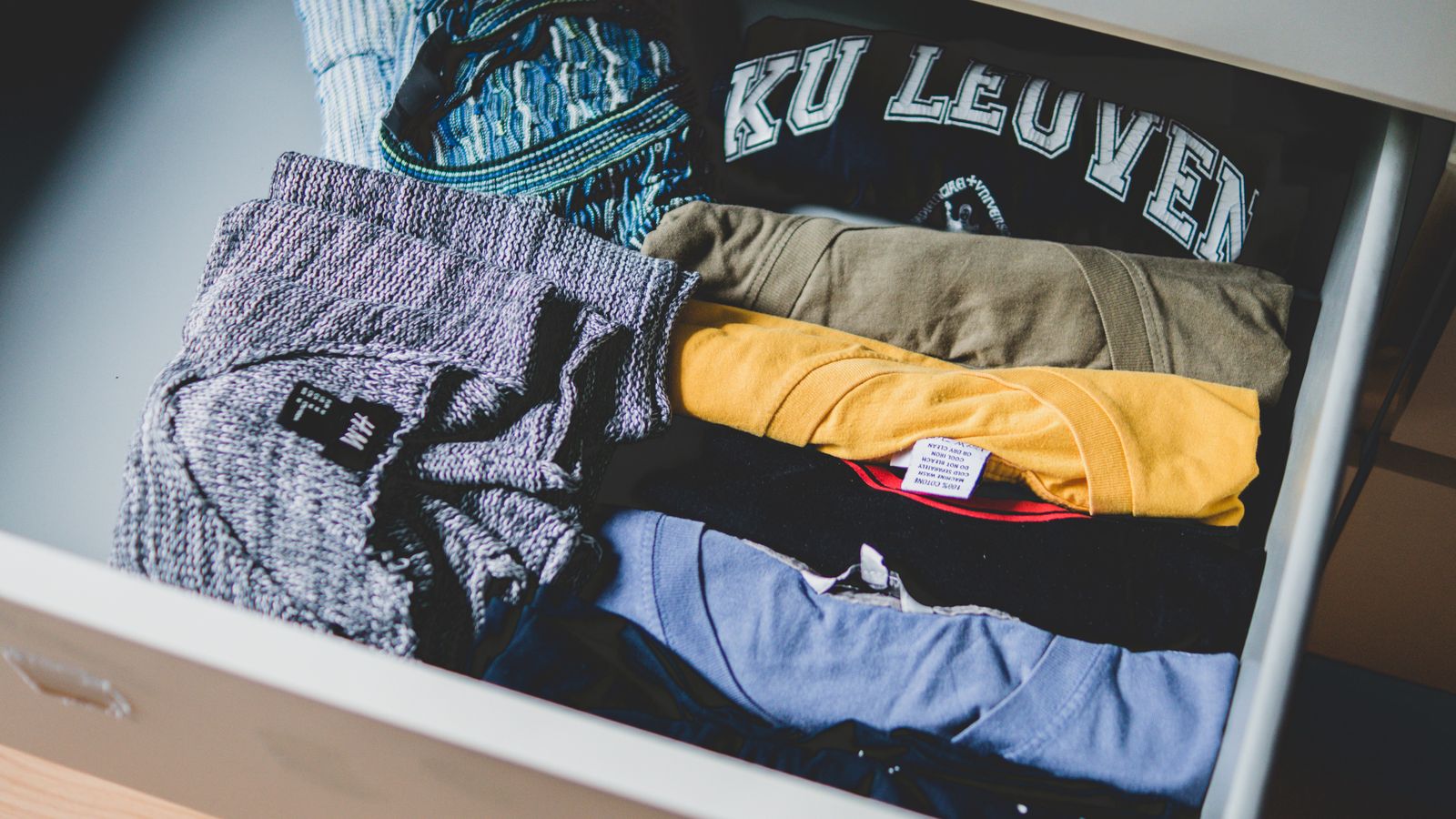 Un tiroir rempli de t-shirts pliés, dont un t-shirt bleu marine sur lequel est imprimé « KU LEUVEN ».